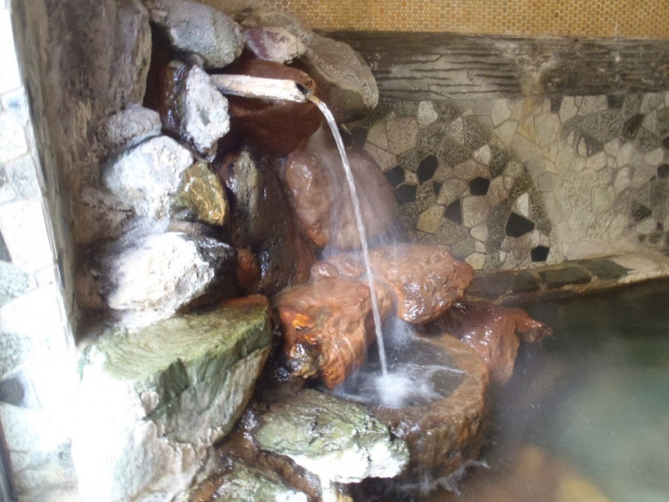 白い石灰質がこびり付いた湯口周りの石と白い湯花が舞う湯中